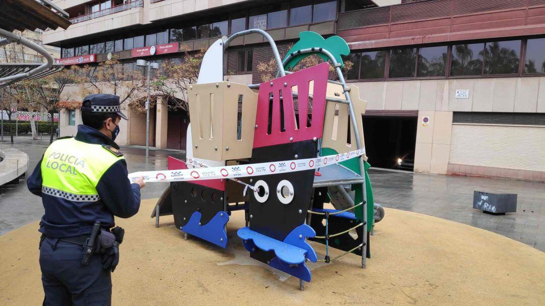 Un agente de la Policía Local precintando unos juegos infantiles en el centro de Alicante