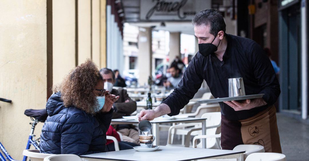 Un camarero sirve un café a una clienta.