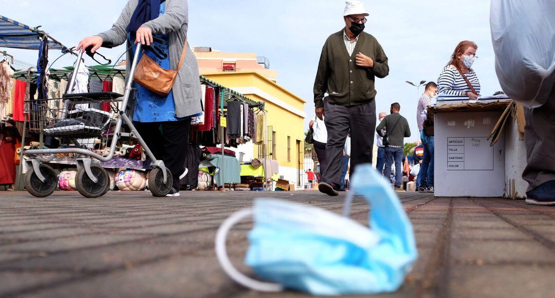 Una mascarilla quirúrgica en el suelo mientras varias personas caminan por un rastro.