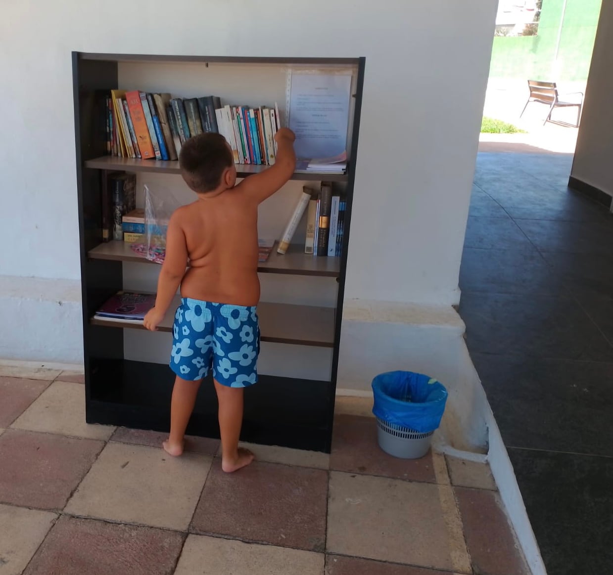 Un niño consulta los libros disponibles en el servicio de préstamo en la piscina municipal de Beniarjó.