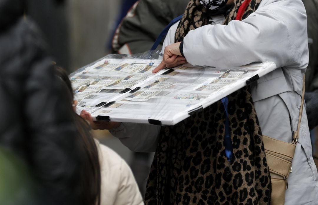 Una personas compra un décimo de lotería de Navidad a una vendedora ambulante