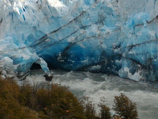 El fenómeno es provocado por el desprendimiento de enormes bloques de hielo por la presión que las aguas del lago Argentino ejercen sobre un dique natural que el Perito Moreno va conformando en su lento avance sobre la costa rocosa.