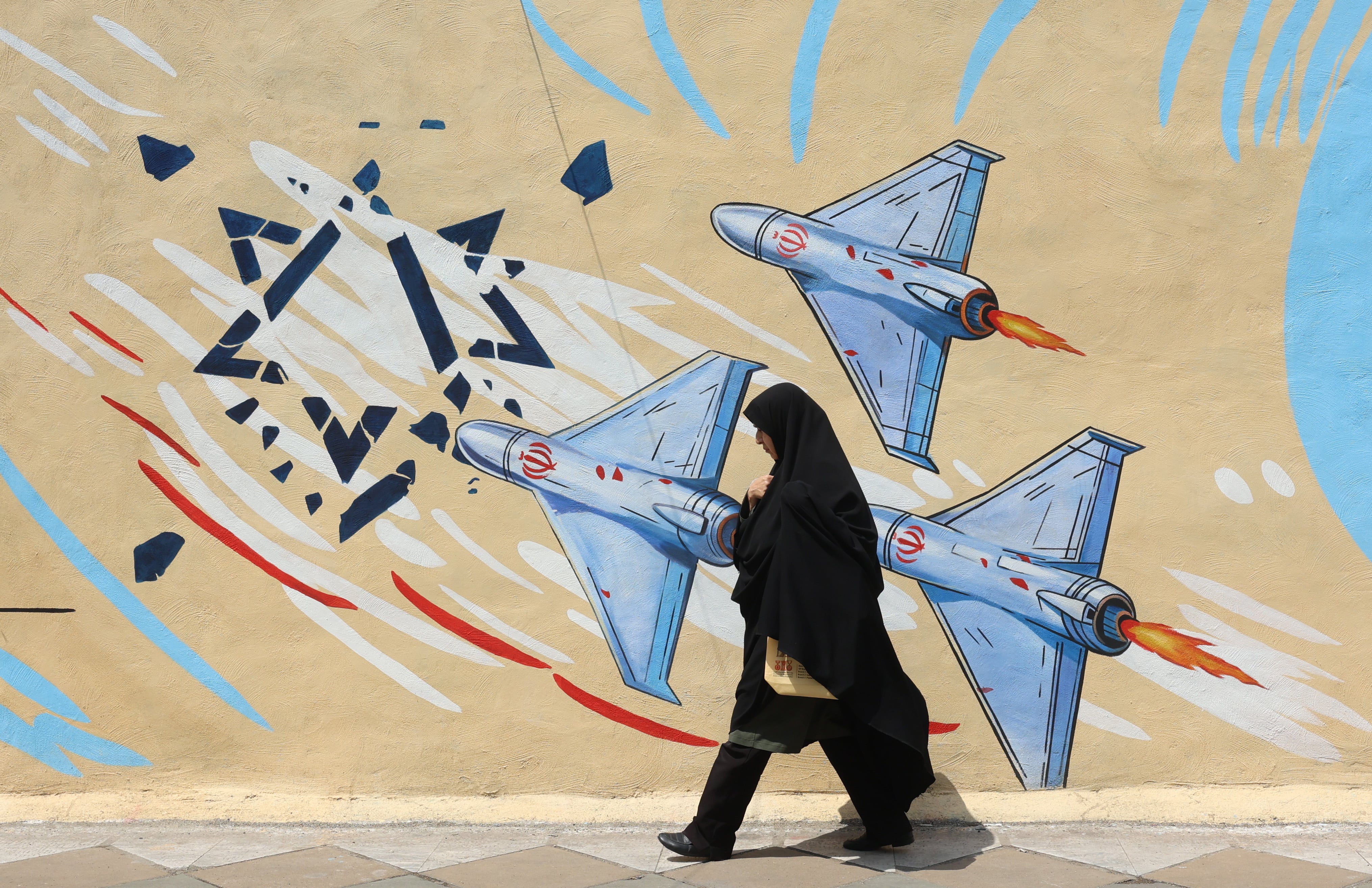Una mujer iraní con velo pasa junto a un mural antiestadounidense y antiisraelí en una calle de Teherán.