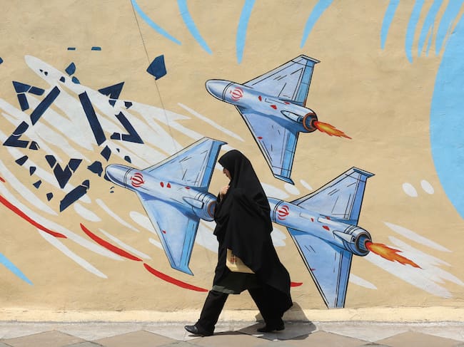 Una mujer iraní con velo pasa junto a un mural antiestadounidense y antiisraelí en una calle de Teherán.