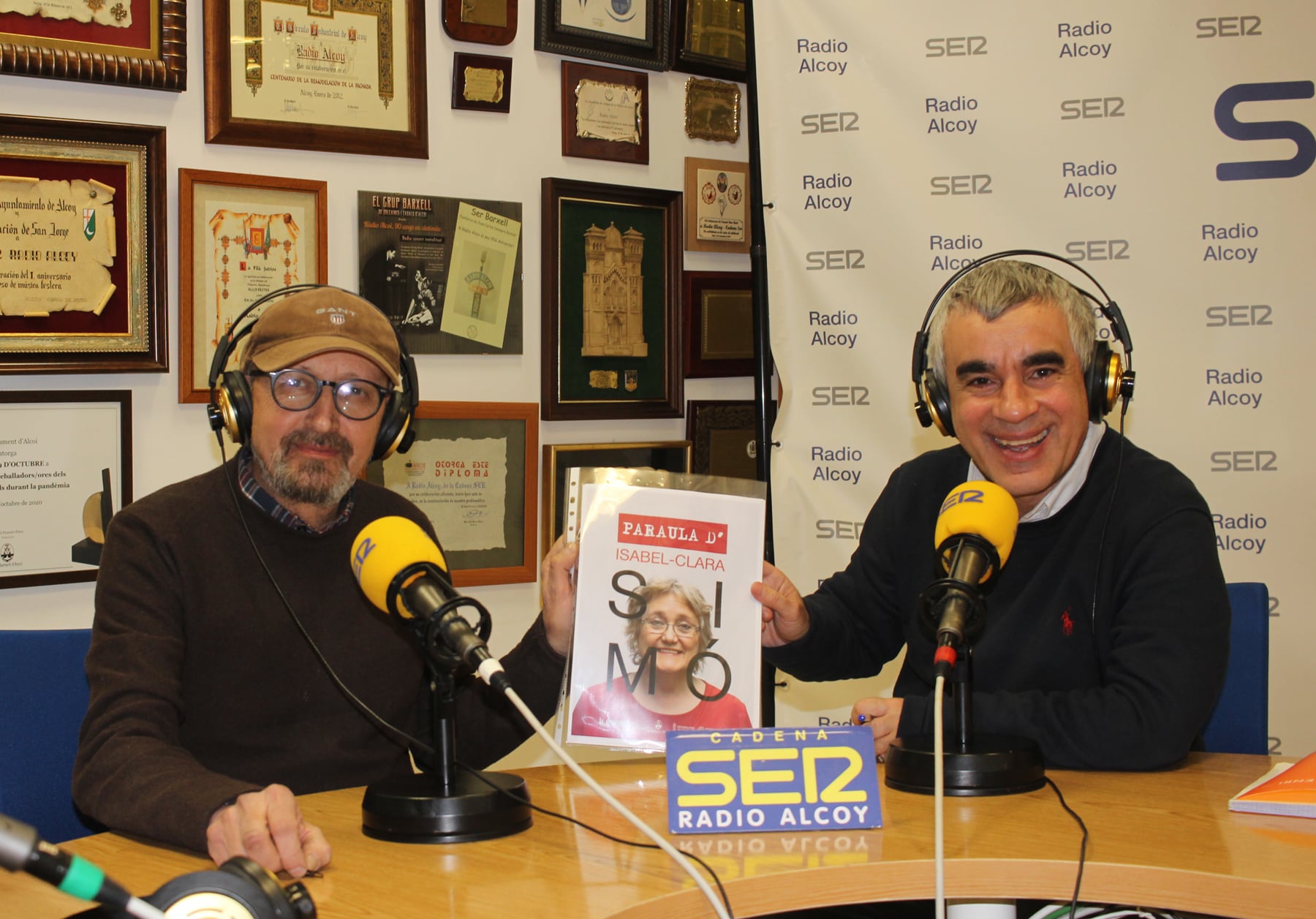 Joanfra Rozalén i Paco Agulló, en l&#039;estudi central de Radio Alcoy, amb un cartell de l&#039;obra &#039;Paraula d&#039;Isabel Clara Simó&#039;