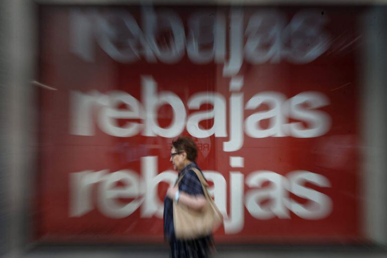 Una mujer pasa delante del escaparate que exhibe un cartel publicitario de un centro comercial en Madrid en el primer día de las rebajas de verano.