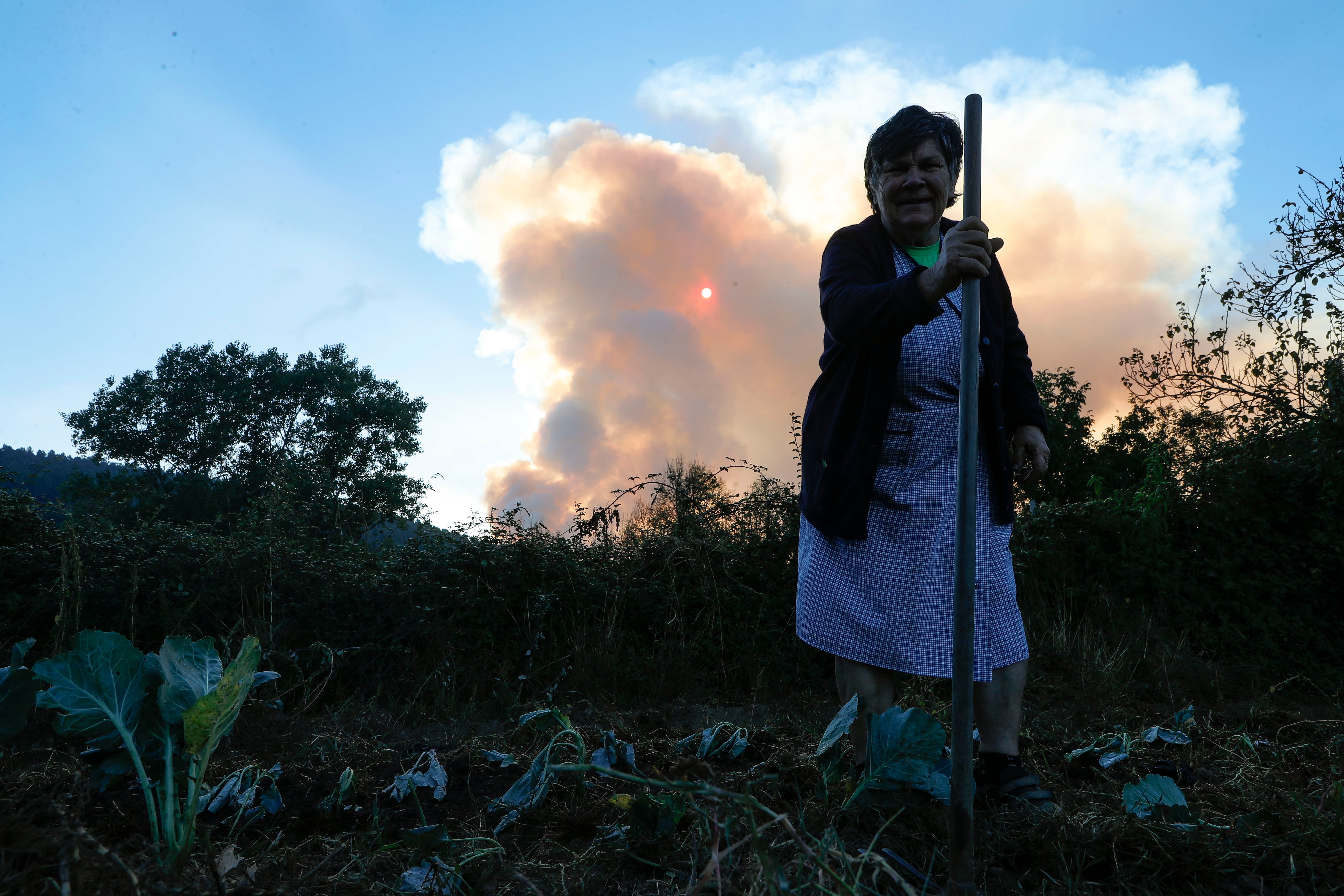A POBRA DO BROLLÓN (LUGO), 26/08/2025.- Una mujer mira la columna de humo desde un pueblo en Pobra de Brollón, Lugo. Galicia tiene este martes tres incendios forestales activos, entre ellos el que se declaró el lunes en A Pobra do Brollón (Lugo), que obligó a activar la situación 2 por su cercanía con núcleos de población y que alcanza las 600 hectáreas. El último balance de Medio Rural recoge que el foco, que ha avanzado 500 hectáreas durante la noche, está próximo a los núcleos de Golmar, en A Pobra do Brollón, y a los de Conceado y San Pedro, en el municipio vecino de Quiroga. EFE/ Eliseo Trigo