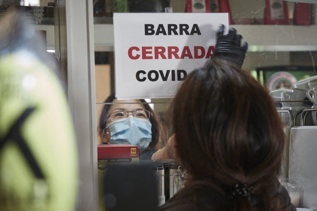 Un camarera coloca un cartel de barra cerrada por Covid