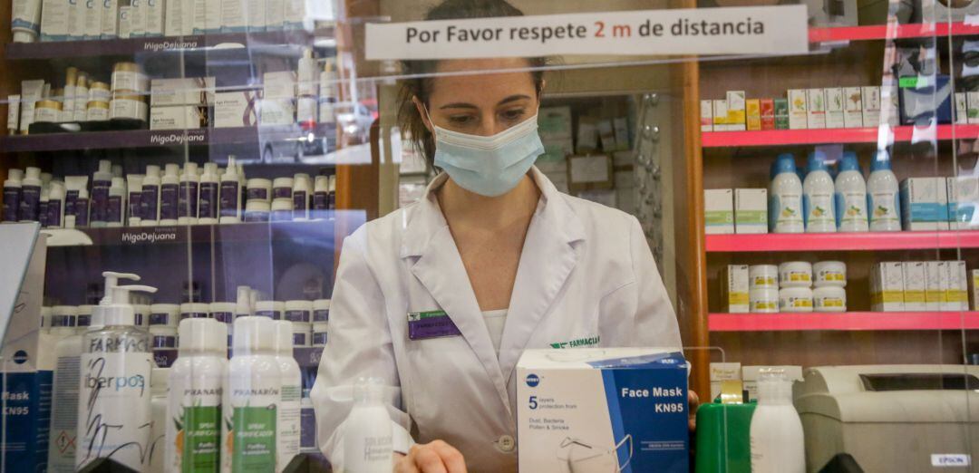 Una farmacéutica tras una mampara y protegida con mascarilla.