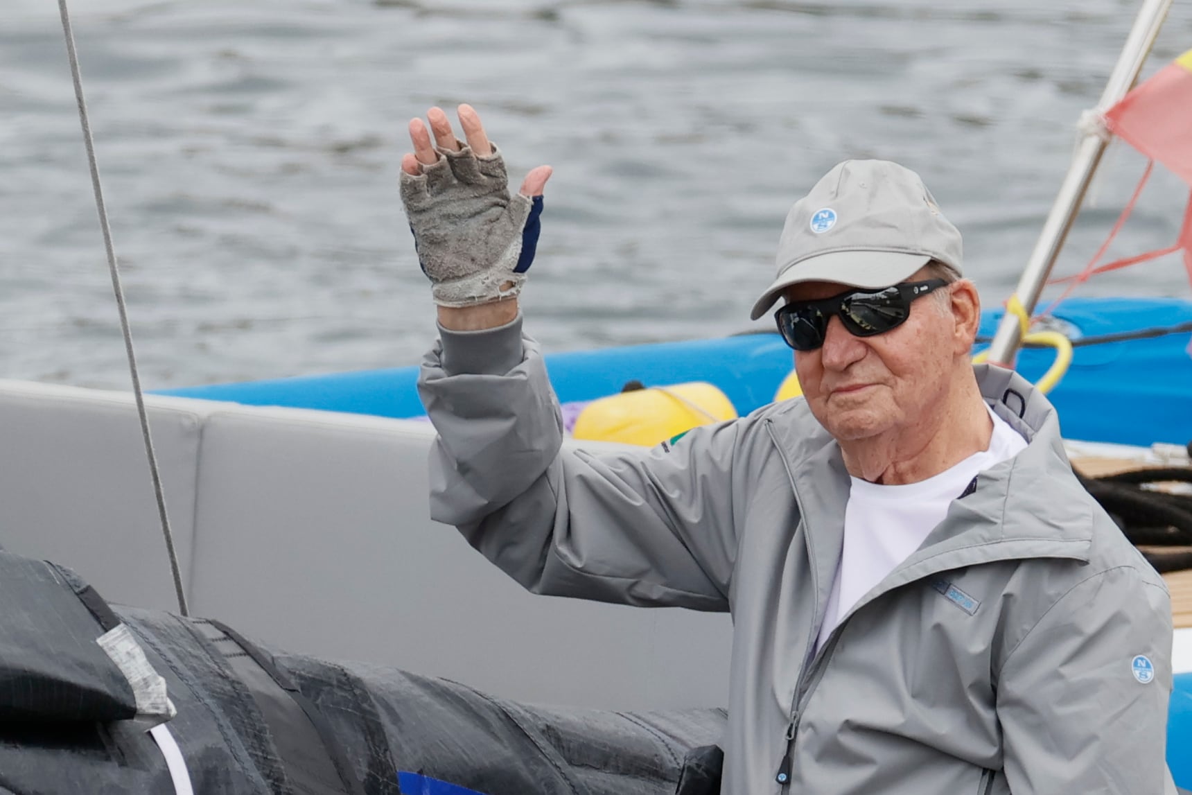 El rey emérito Juan Carlos I saluda desde la embarcación a su llegada este jueves al Real Club Náutico de Sanxenxo.