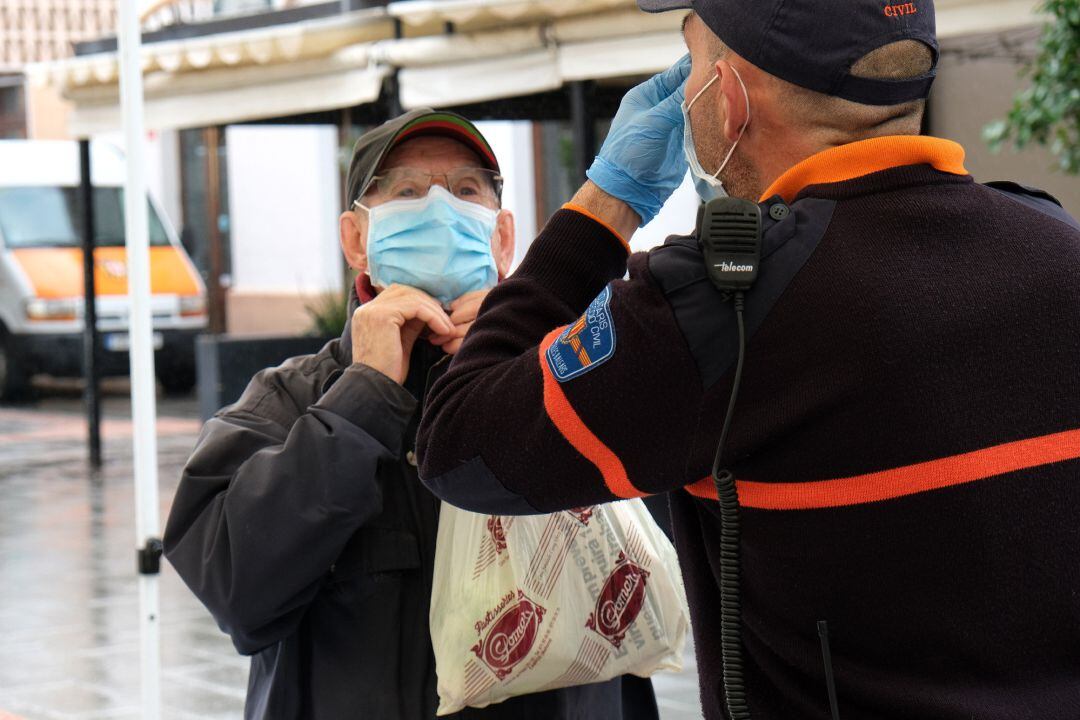 Un hombre recibe las indicaciones de cómo colocarse la mascarilla por parte de un agente local 