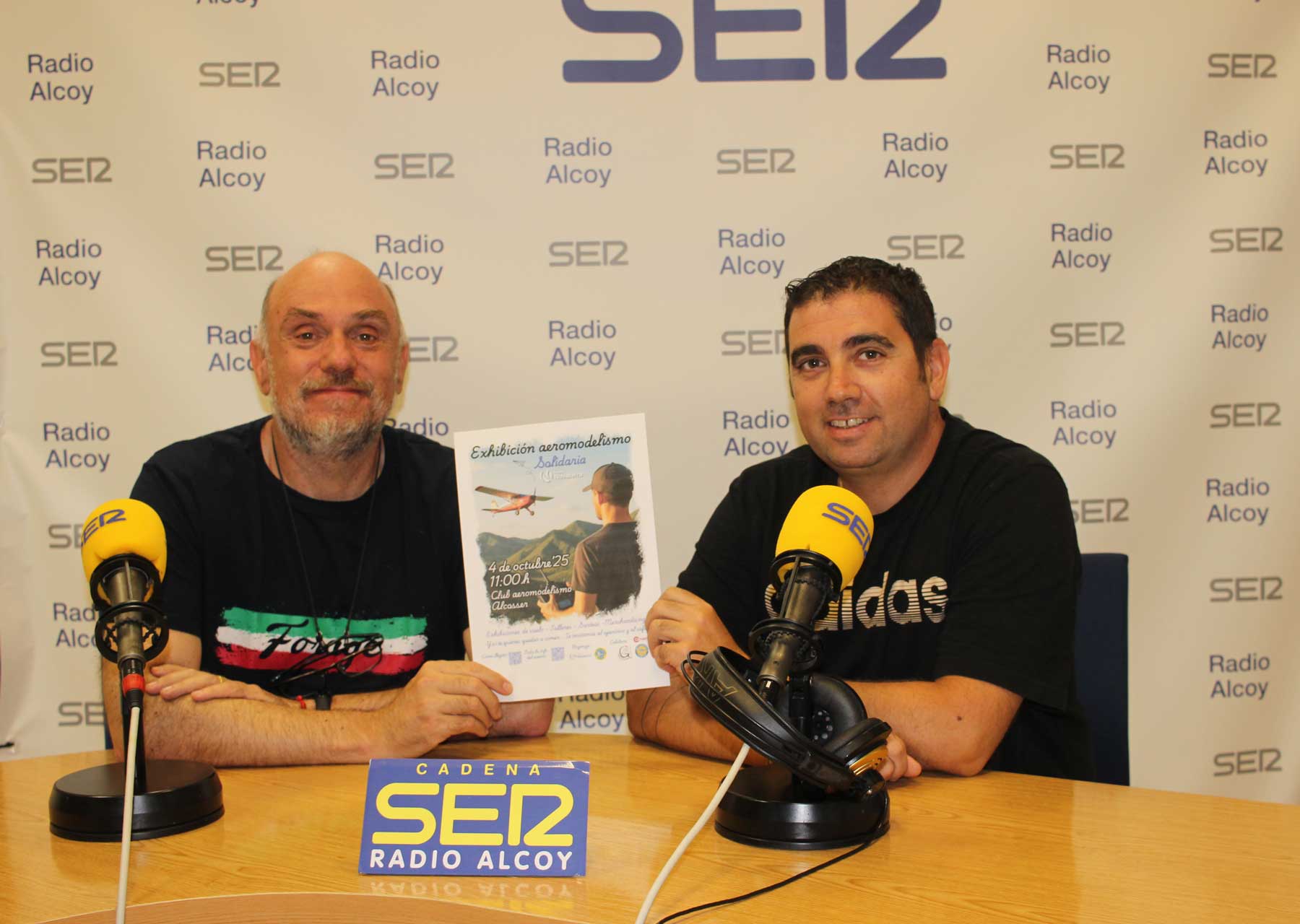 Gabi Barrachina y Carlos Escuder, en el estudio central de Radio Alcoy, con un cartel de la actividad solidaria