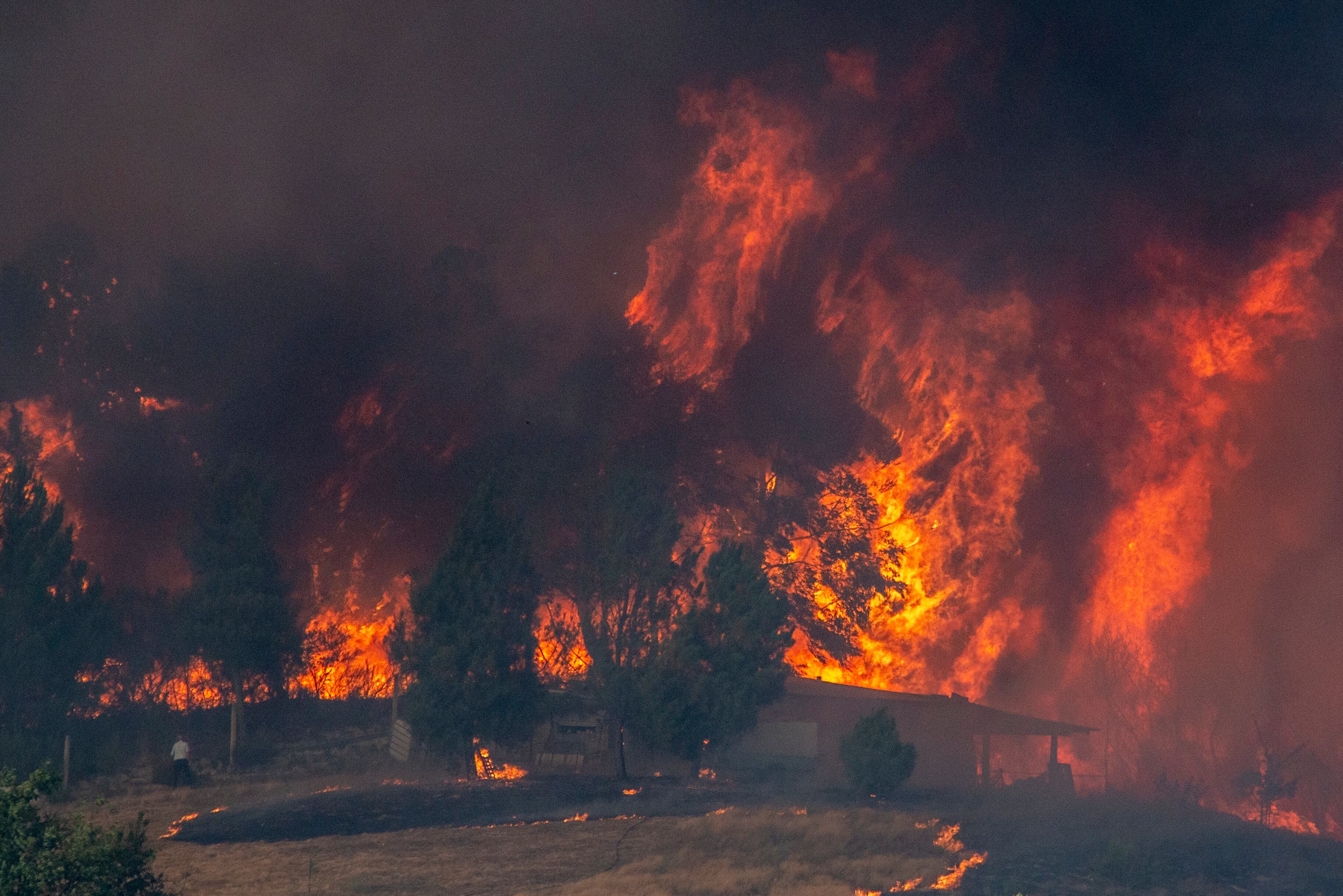 Vista de las llamas del incendio forestal que permanece activo en Verín (Ourense) cerca de una construcción.