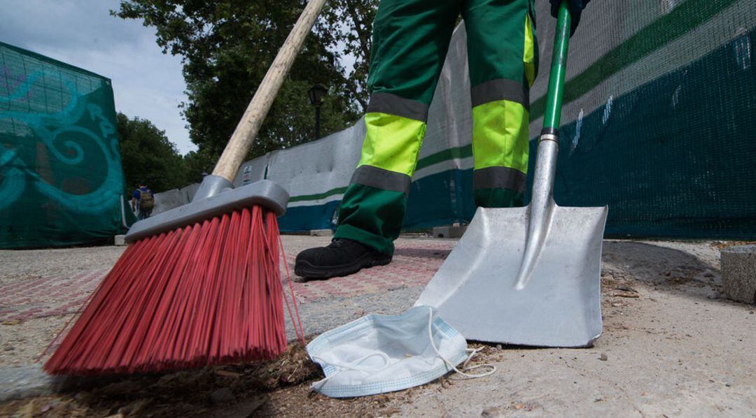Personal de limpieza municipal barre una mascarilla del suelo.