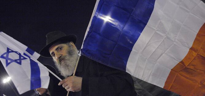 Un hombre sostiene una bandara francesa y otra israelí durante el minuto de silencio que París dedicó a las víctimas del colegio judío en Toulouse