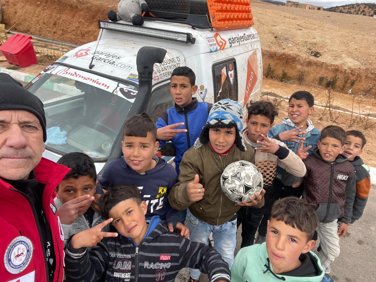 Fernando García posa ante el coche y niños que viven en las zonas que recorre el raid