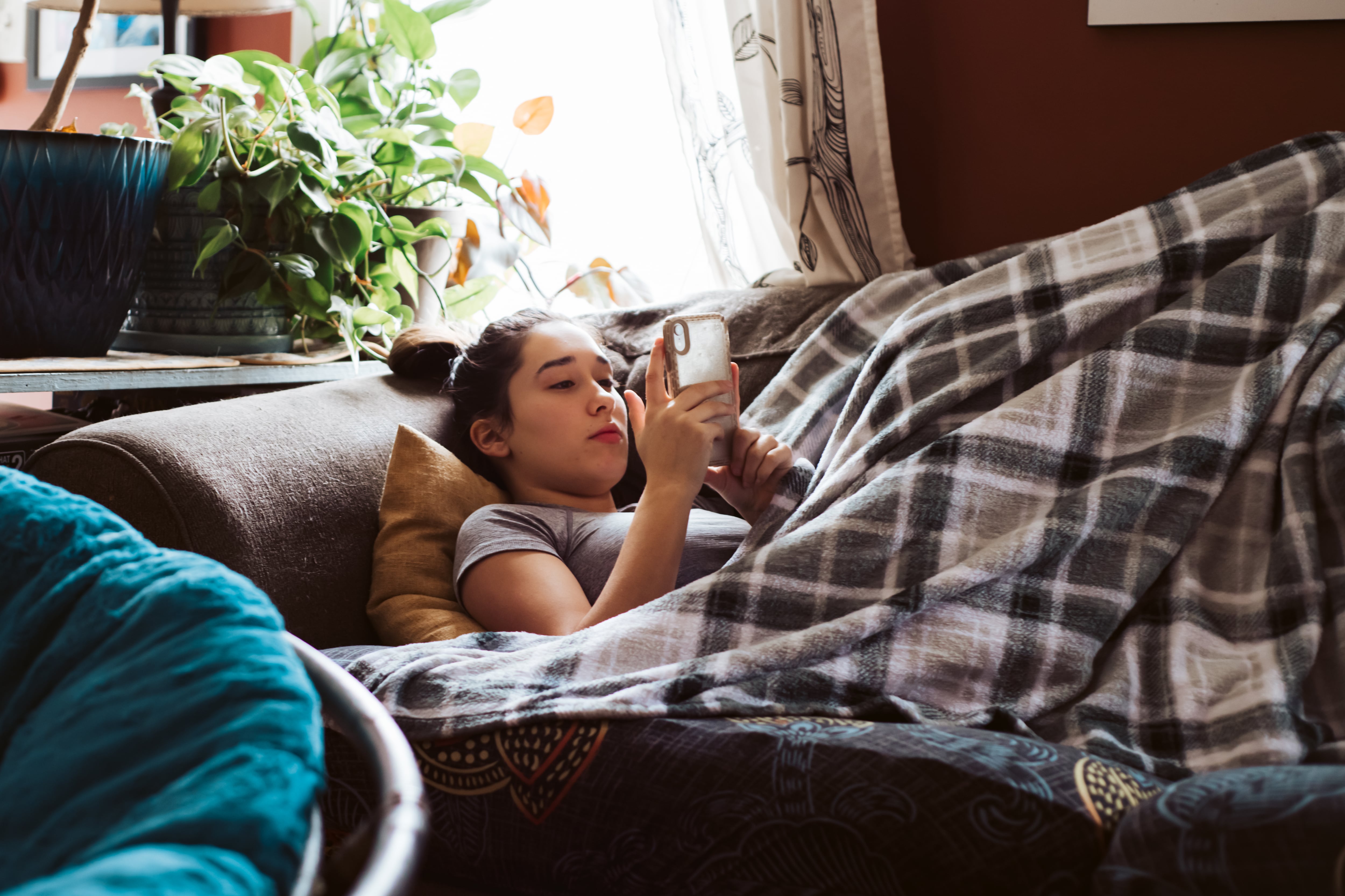 Una adolescentes, tirada en el sofá viendo el móvil