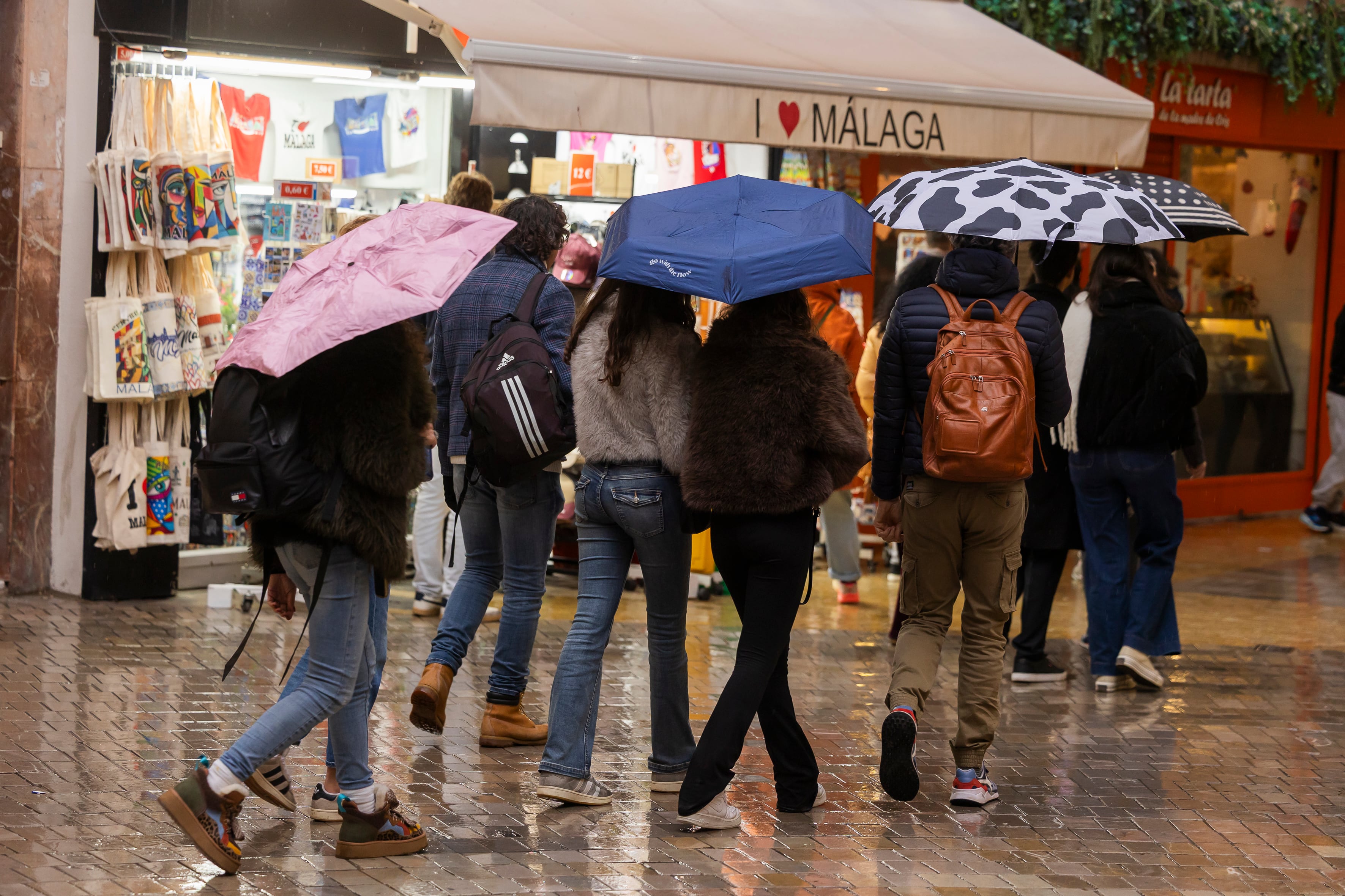 Un grupo de personas con sus paraguas en el centro de Málaga este sábado, que se encuentra desde las 15.00 hasta las 4:00 de la madrugada en alerta roja por lluvias. EFE / Carlos Díaz.