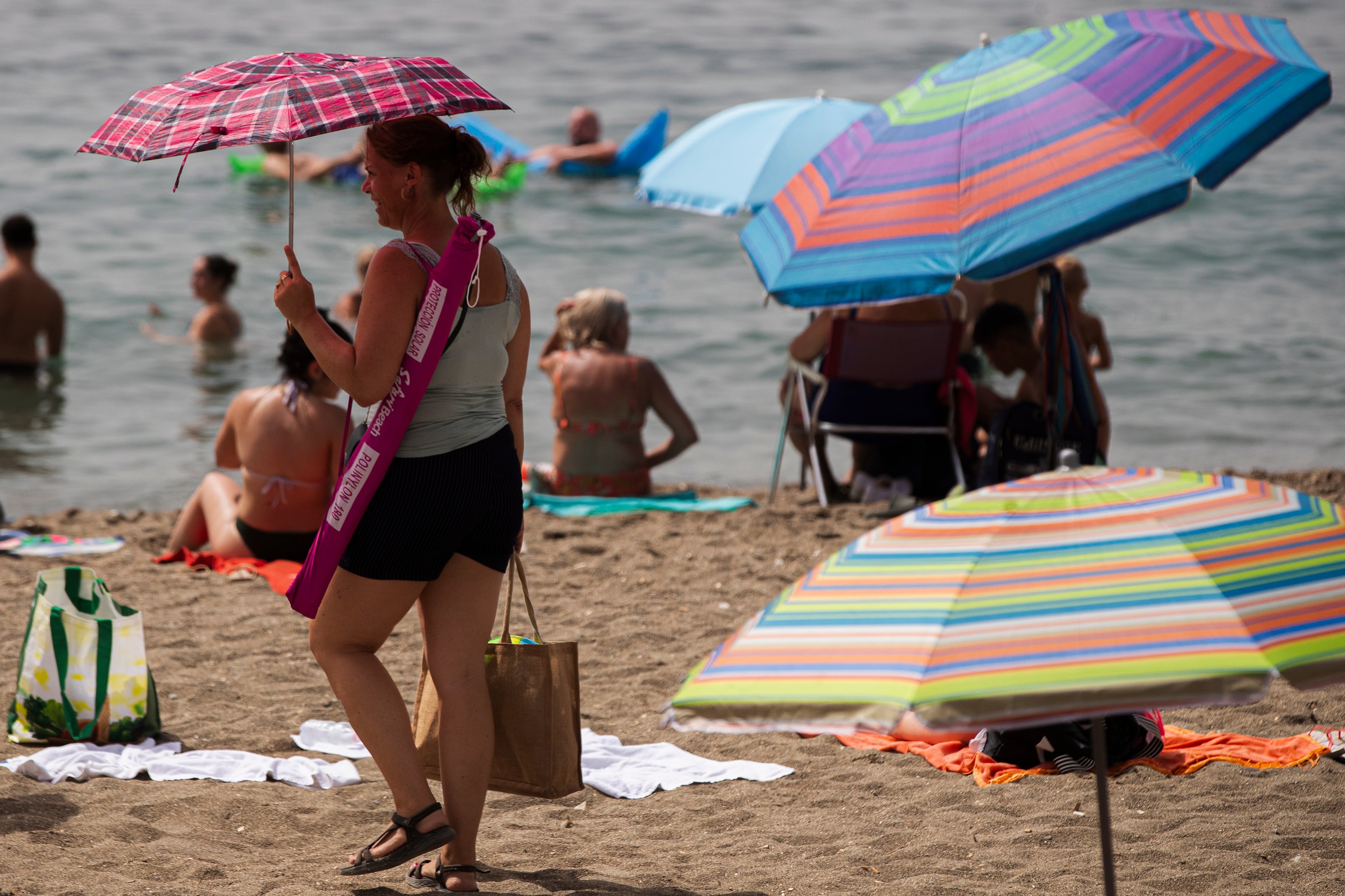 Una mujer con una sombrilla camina buscando sitio en la playa. Archivo.