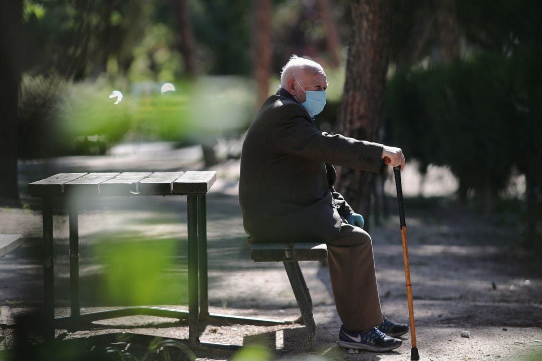 Un anciano con mascarilla descansa en un parque