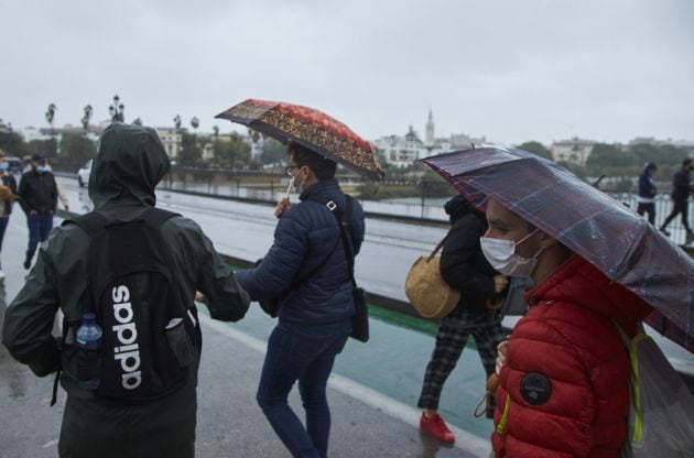 Un grupo de personas cruzando el Puente de Isabel II en un día lluvioso del puente de Todos los Santos en Sevilla.