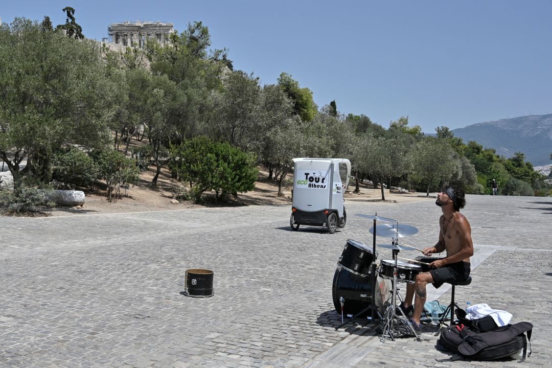 Un músico callejero toca completamente solo en una zona turística de Atenas, este jueves, con temperaturas de hasta 44 grados.