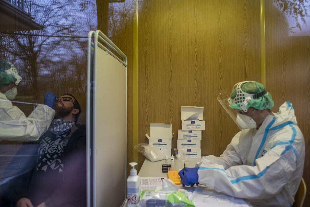 Un trabajador sanitario toma una muestra con un hisopo para una prueba de antígenos mientras otro organiza los tubos con muestras durante un cribado. Imagen de archivo