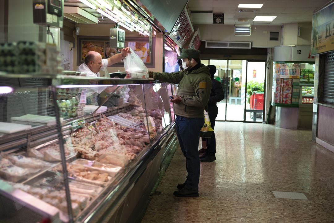 Un vendedor de carne en un mercado da la bolsa con la compra a un cliente, que lleva una mascarilla por la pandemia del coronavirus