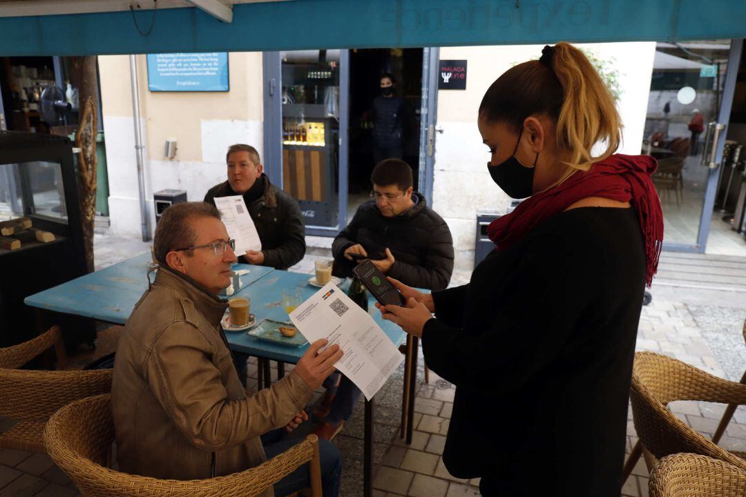 Una camarera pide certificado a los clientes en una mesa en la terraza de un bar durante el primer día de petición de Certificados COVID.