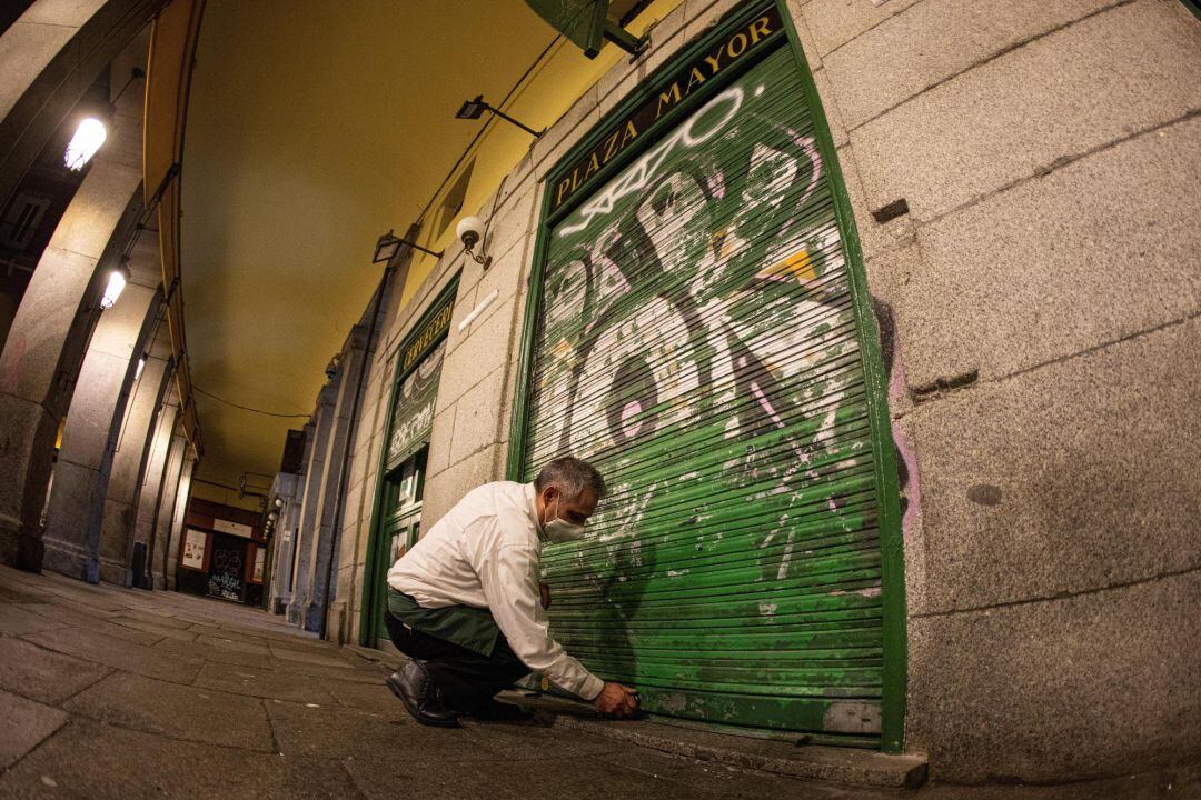 Un hombre cierra la puerta de su negocio antes de la hora límite establecida en Madrid