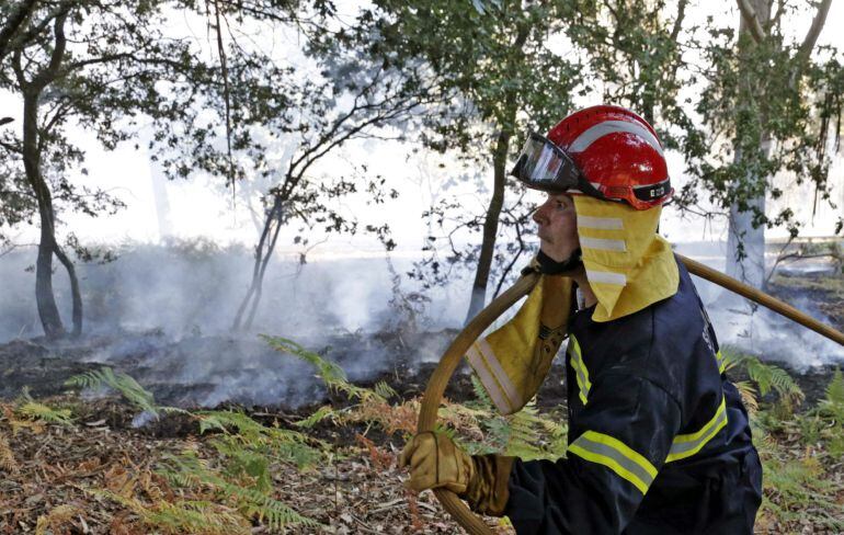 GRA141. TEO (A CORUÑA), 09/08/2015.- Un bombero carga con la manguera tras la extinción de un incendio forestal cerca de unas viviendas en Cacheiras, en la localidad de Teo (A Coruña), esta tarde muy cerca de Santiago de Compostela. EFE/Lavandeira jr.