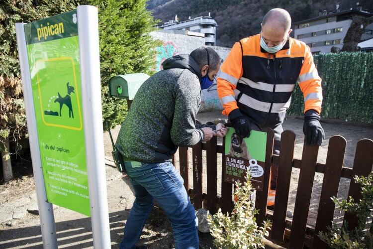 Dos operaris del comú d'Andorra la Vella instal·lant un cartell sobre l'ADN caní en un pipican de la parròquia