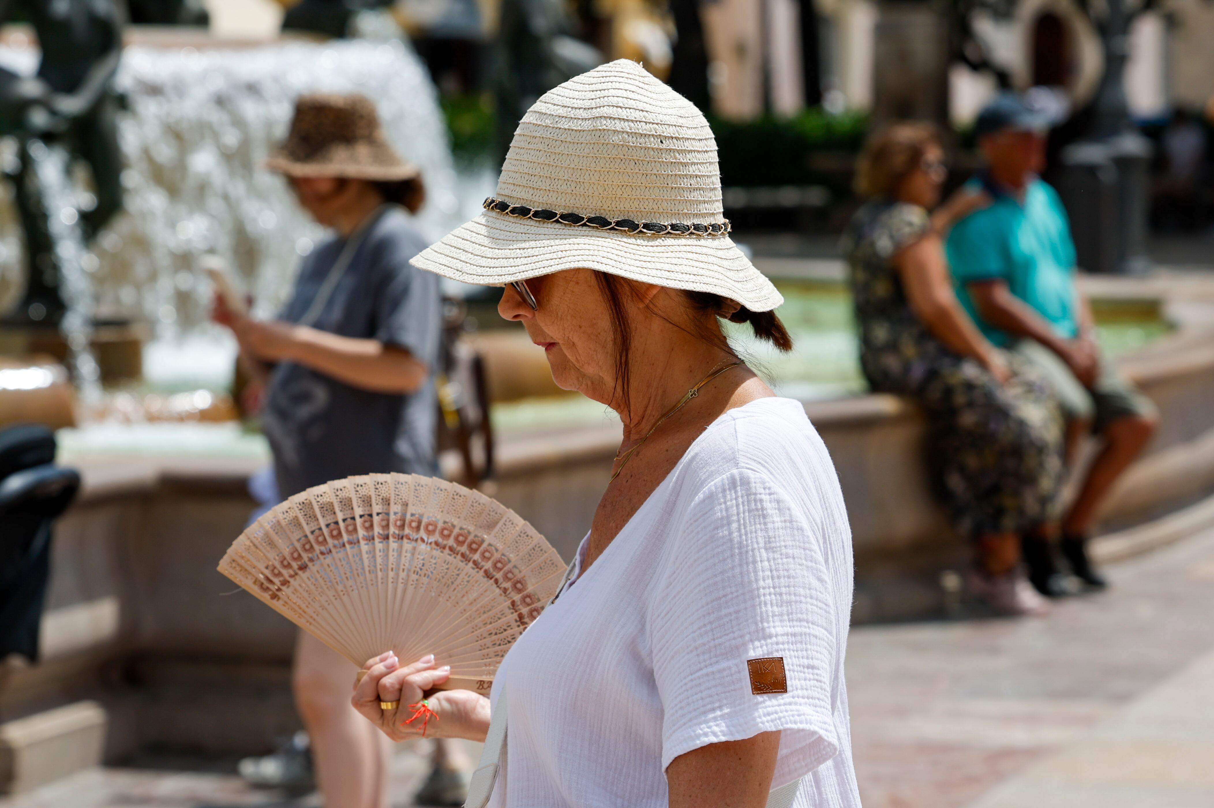 GRAFCVA8125. VALENCIA, 12/06/2025.- Una mujer se protege del sol y calor con sombrero y abanico durante este jueves en el que se viven temperaturas veraniegas en la Comunidad. EFE/Ana Escobar