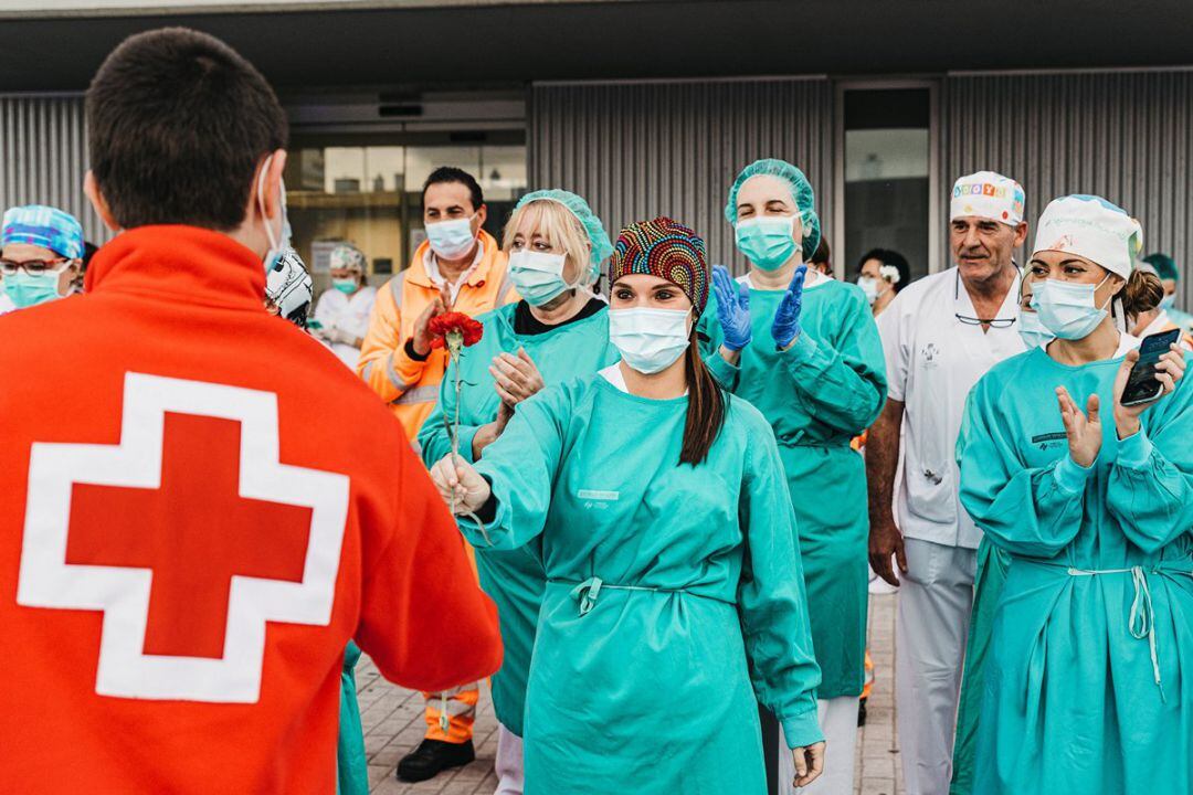 Un voluntario de la Cruz Roja entrega un clavel a una sanitaria del hospital de Gandia