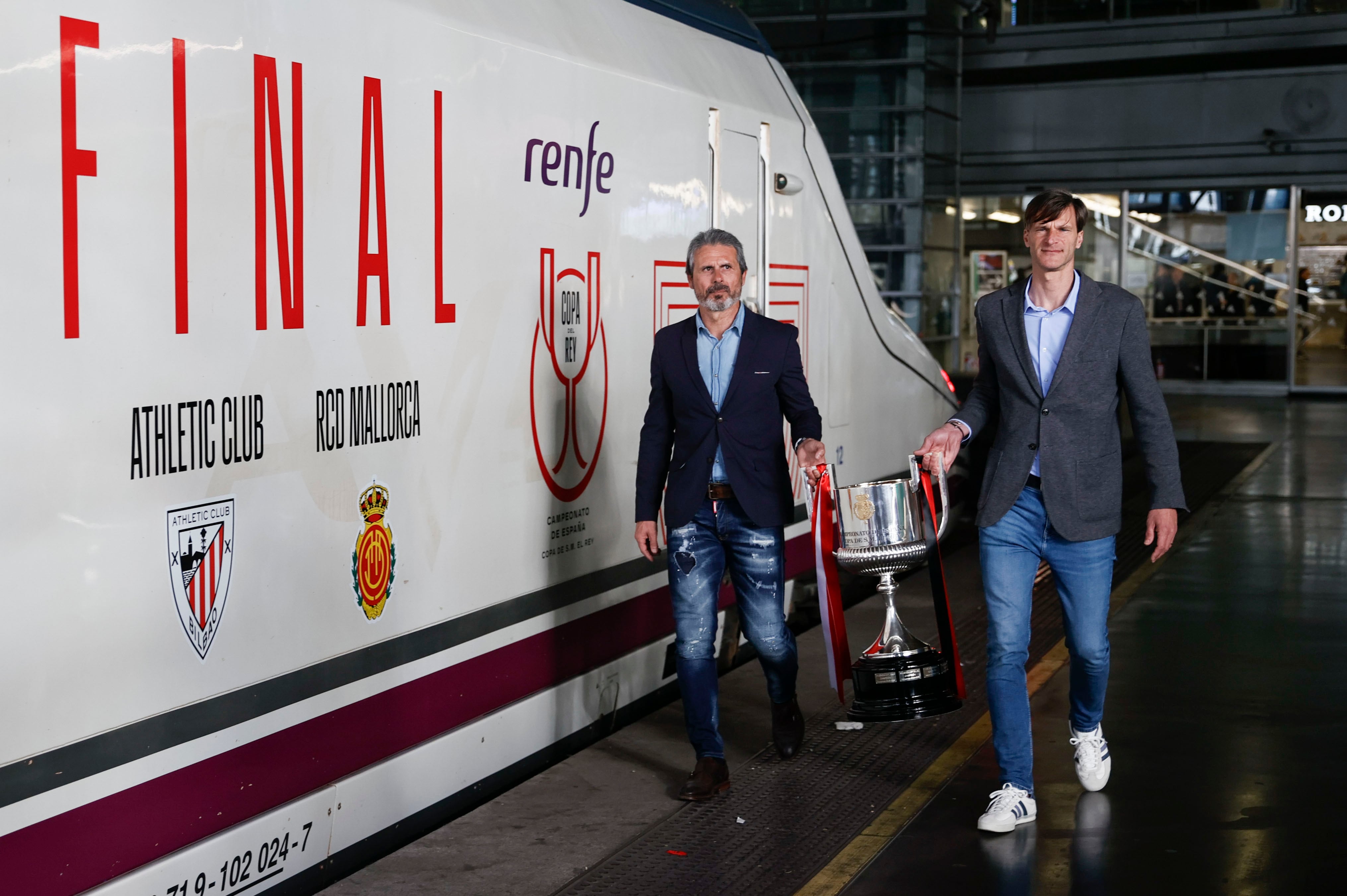 Los exfutbolistas Rafael Alkorta, en representación del Athletic Club, y Leo Franco, en representación del Mallorca, cargan con la Copa del Rey en la estación de Atocha en Madrid durante su traslado a Sevilla con motivo de la final. EFE/ Fernando Alvarado