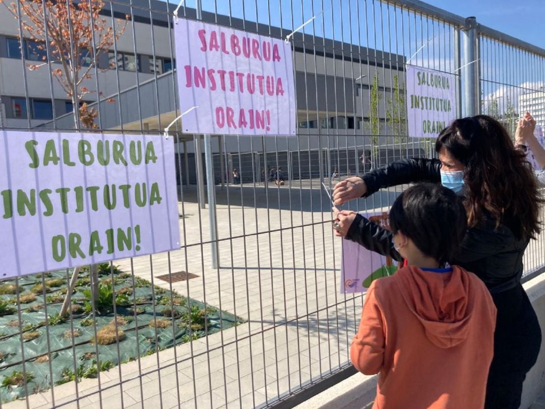 Un alumno de Ekabarri y una madre de los alumnos del colegio cuelgan carteles bajo el lema "instituto de Salburua ya" en las verjas de la puerta principal del colegio.