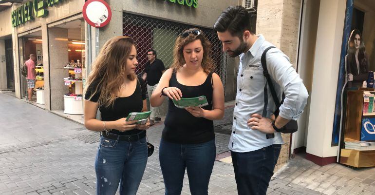 Cristina Liébana, de las Juventudes Socialistas de Jaén (izqda) y Azahara Cabrera, secretaria de organización de las JSA de Andalucía (centro), entregan a un joven un folleto de la campaña.