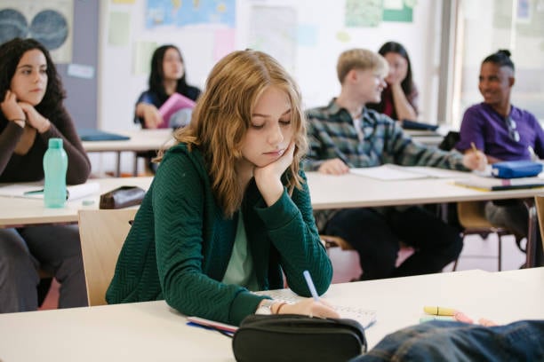 A student concentrating and taking notes while working in a classroom with her classmates.