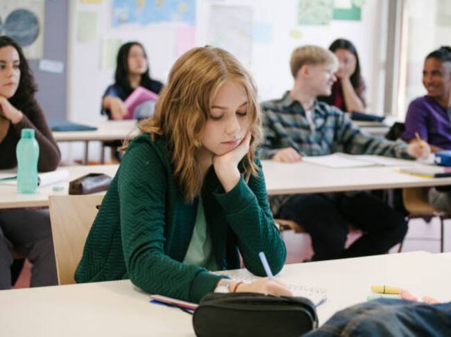A student concentrating and taking notes while working in a classroom with her classmates.
