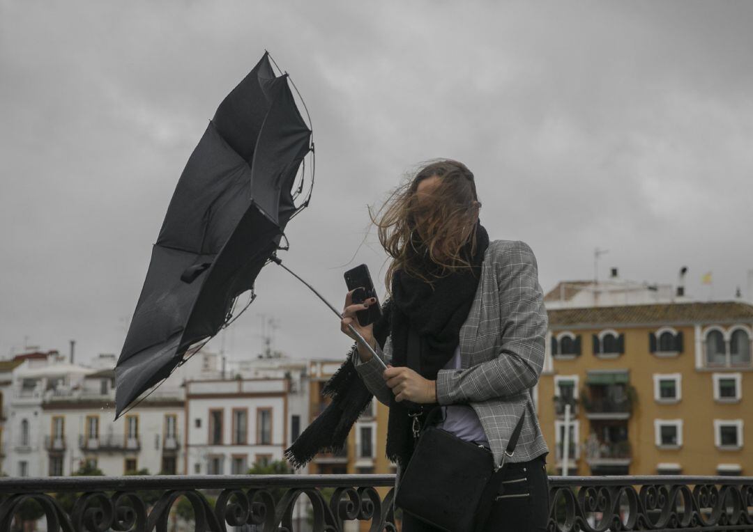 Una racha de viento desbarata el paragüas de una viandante mientras camina por el Puente de Isabel II, en Sevilla.