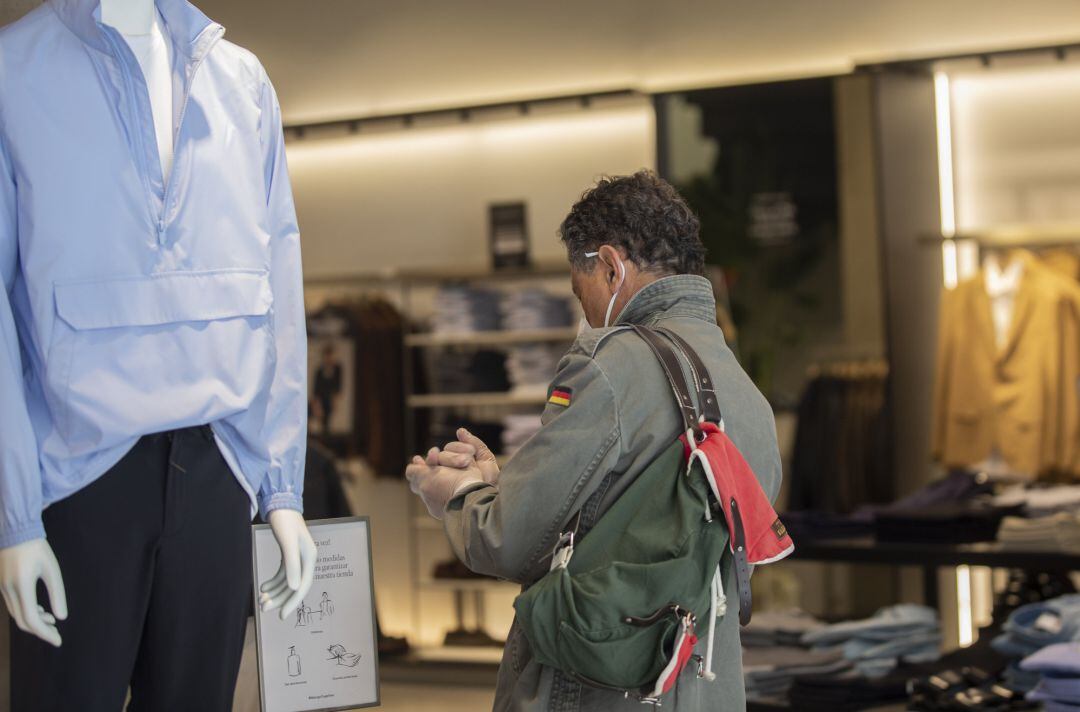 Un hombre se desinfecta unos guantes proporcionados en la entrada de una tienda de ropa, durante el segundo día de la fase 1 del plan de desescalada que ha elaborado el Gobierno de España. En Sevilla, (Andalucía, España), a 12 de mayo de 2020. 12 MAYO 2020
 