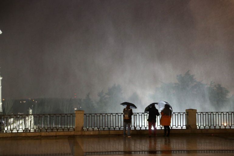 Varias personas observando las partículas de agua en suspensión debido al fuerte viento en la Plaza de Oriente, junto al Palacio Real de Madrid