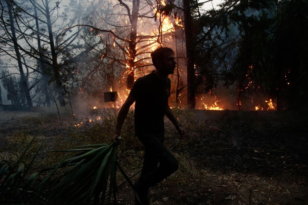 Un policía local  intenta extinguir un incendio en la zona de Varybobi, al noeste de Atenas, este martes.