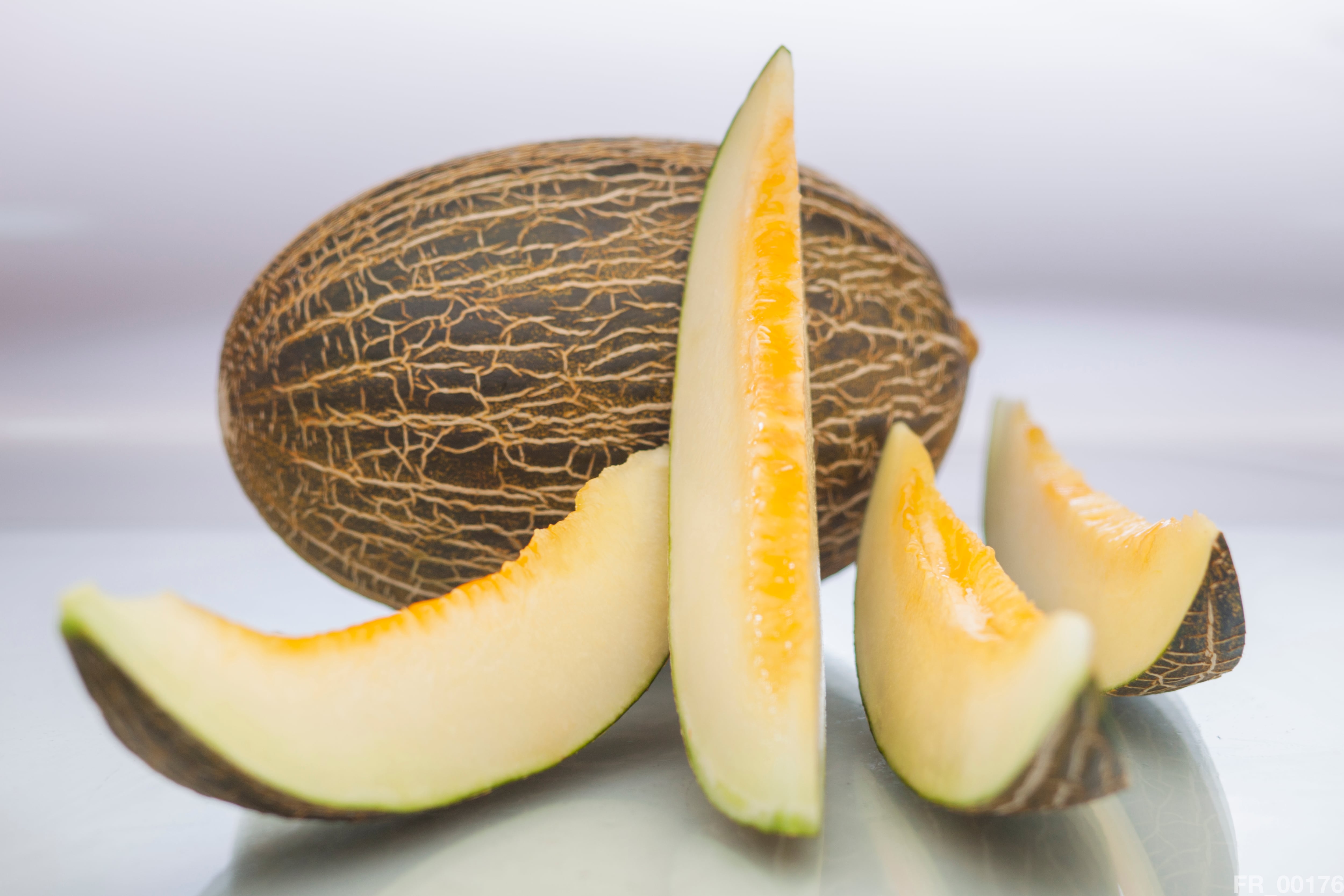 Simple composition of an entire melon with four slices by side on white background