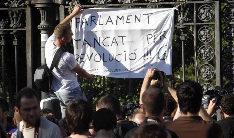 Una persona cuelga una pancarta donde puede leerse &quot;Parlament tancat per revolució&quot;, durante las protestas protagonizadas por miles de indignados en 2011.