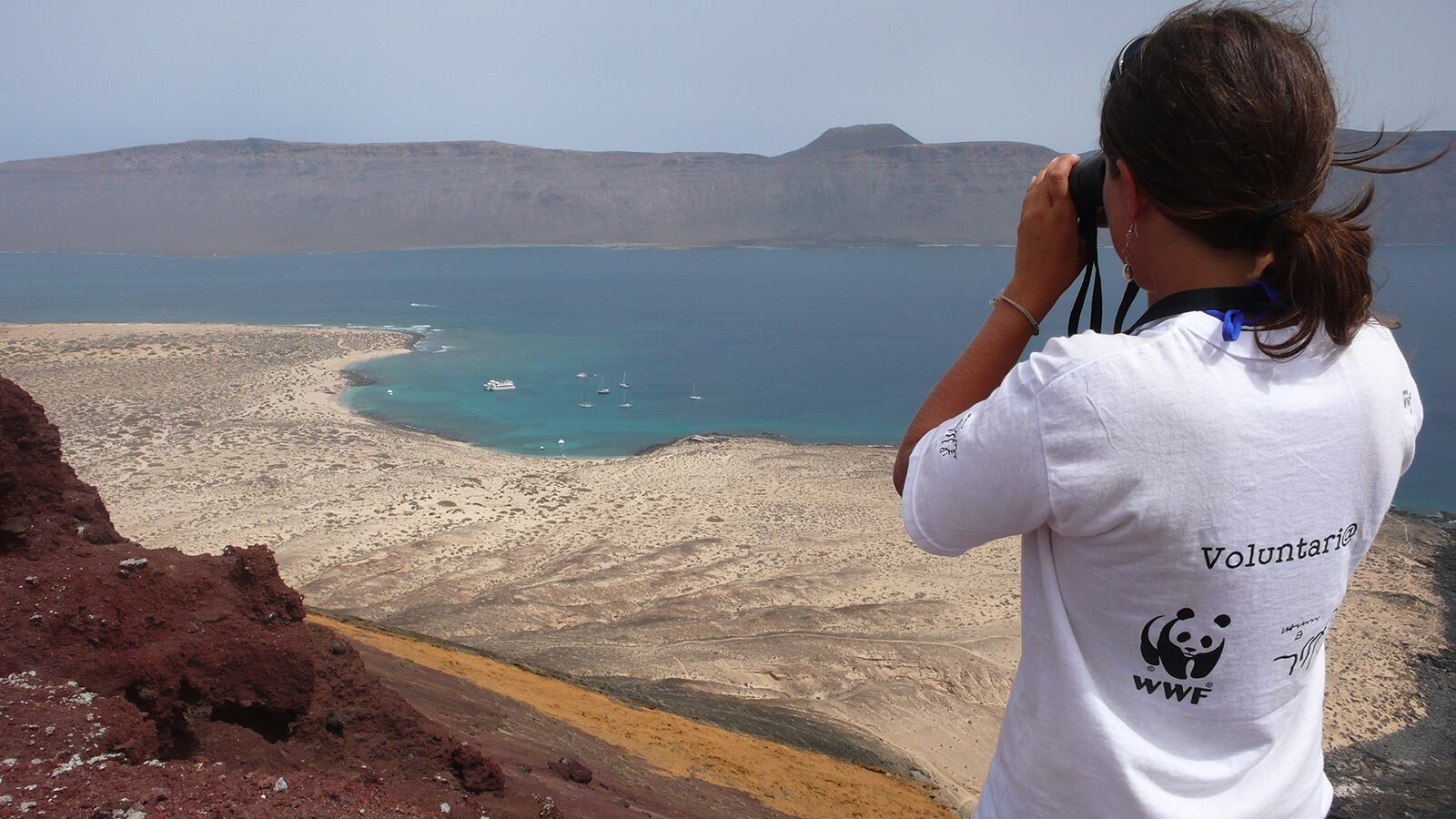 Una voluntaria de WWF vigila en la isla de La Graciosa (Archipiélago Chinijo) que no se realicen actividades no permitidas en el Parque Natural Archipiélago Chinijo, como la pesca submarina. Al fondo, Lanzarote.