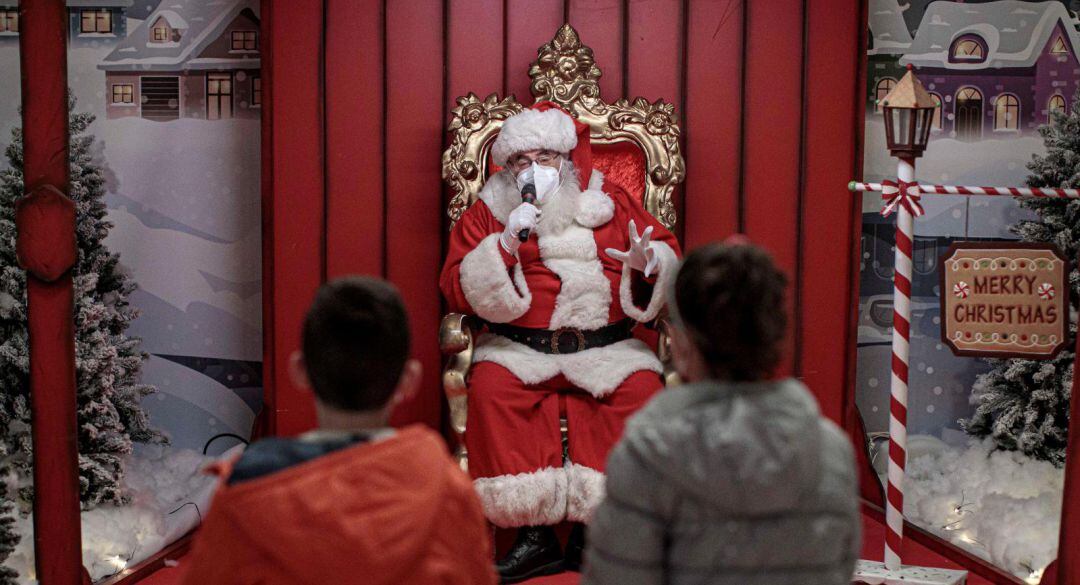 Una persona vestida de Papá Noel con mascarilla conversa con unos niños en València