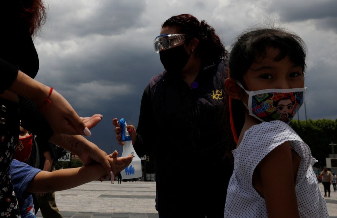 Una niña con mascarilla espera para que personal de servicio le reparta gen desinfectante a las puertas de la Basílica de Guadalupe, en Ciudad de Mexico.