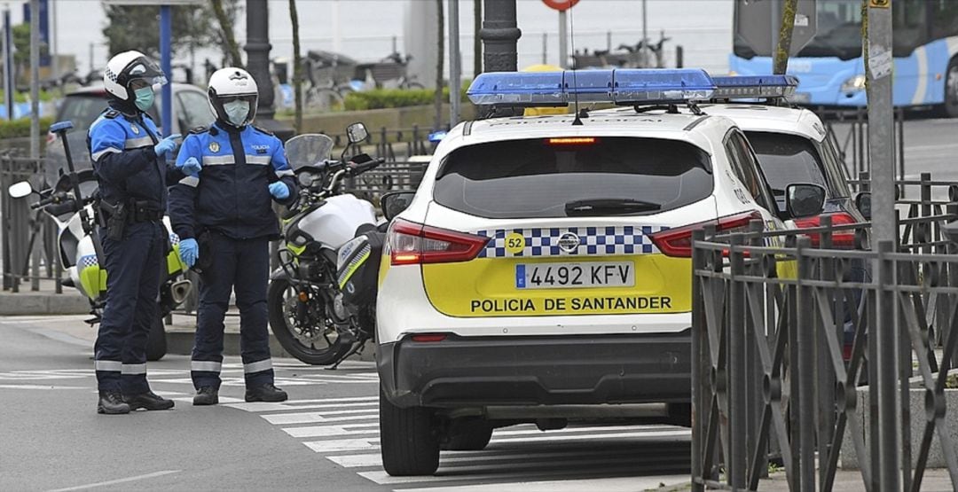 Dos agentes de Policia Local en Santander junto a varios vehículos policiales.