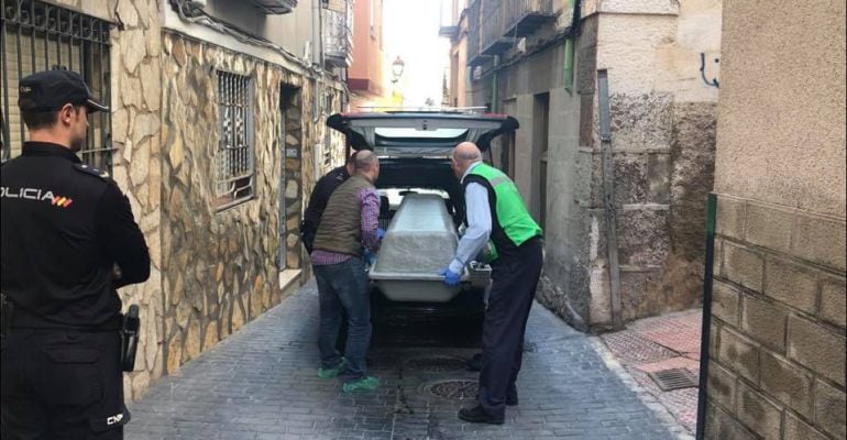 Agentes de la Policía Nacional y personal de los servicios funerarios introducen el cuerpo del fallecido en el coche fúnebre.